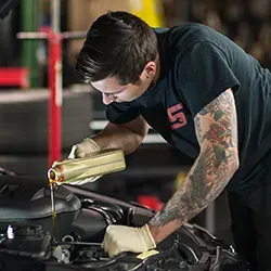 Mechanic wearing gloves pours oil into a car engine, in a garage.