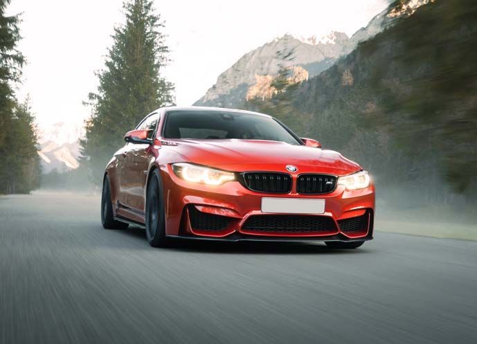 A red bmw m4 is driving down a mountain road.
