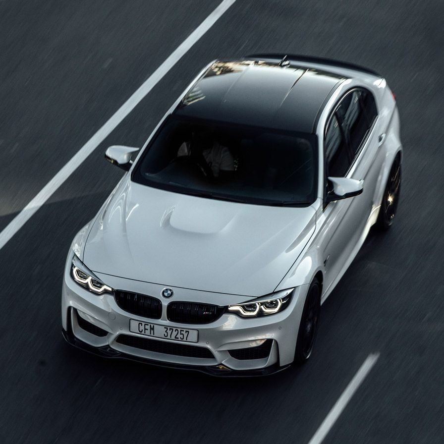 A white bmw with a black roof is driving down a road