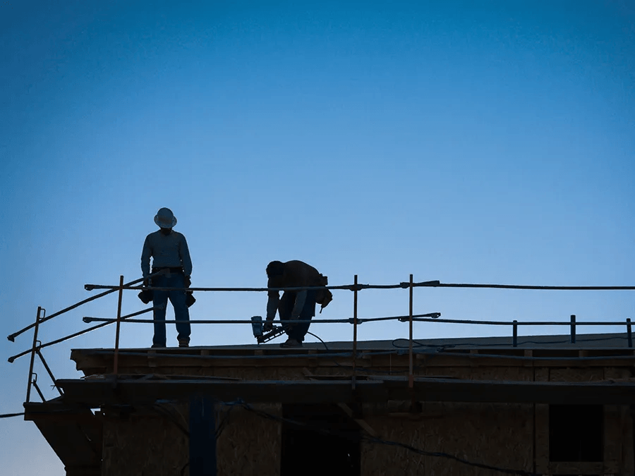 Two construction workers are working on the roof of a building.