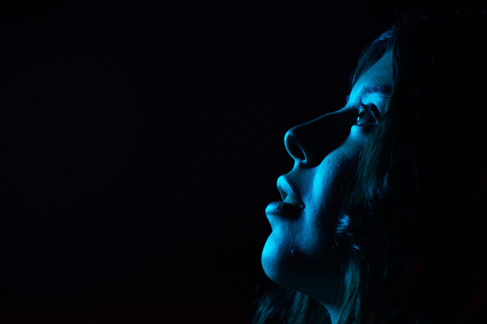 A woman looking at a blue light screen in a dark room.