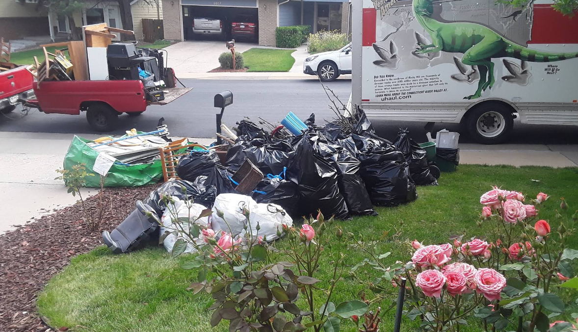 A truck with a t-rex on it is parked in front of a pile of trash.