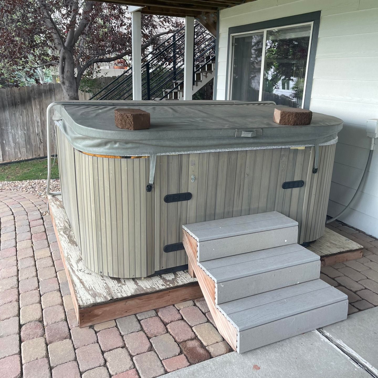 A hot tub is sitting on a brick patio next to stairs.