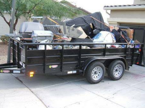 A trailer full of junk is parked in front of a house.