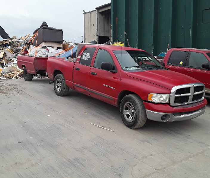 A red dodge ram truck is pulling a trailer full of garbage