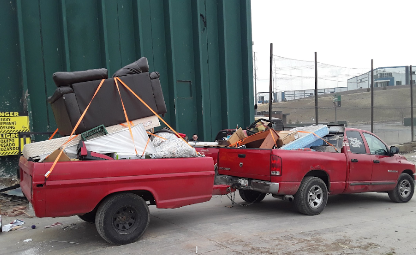 A red truck is pulling a trailer full of furniture.