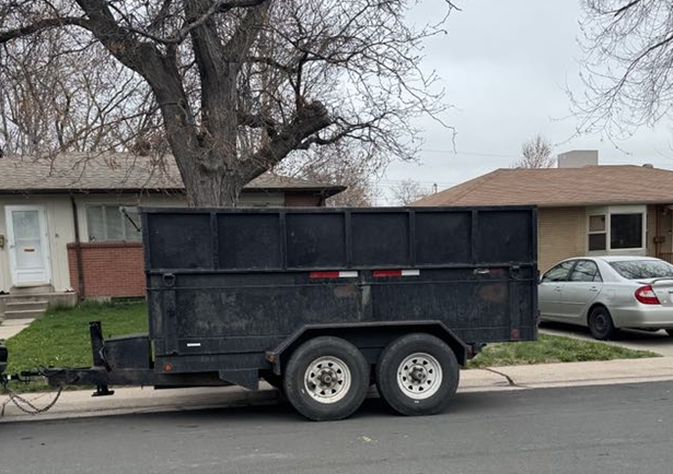A dumpster trailer is parked on the side of the road in front of a house.