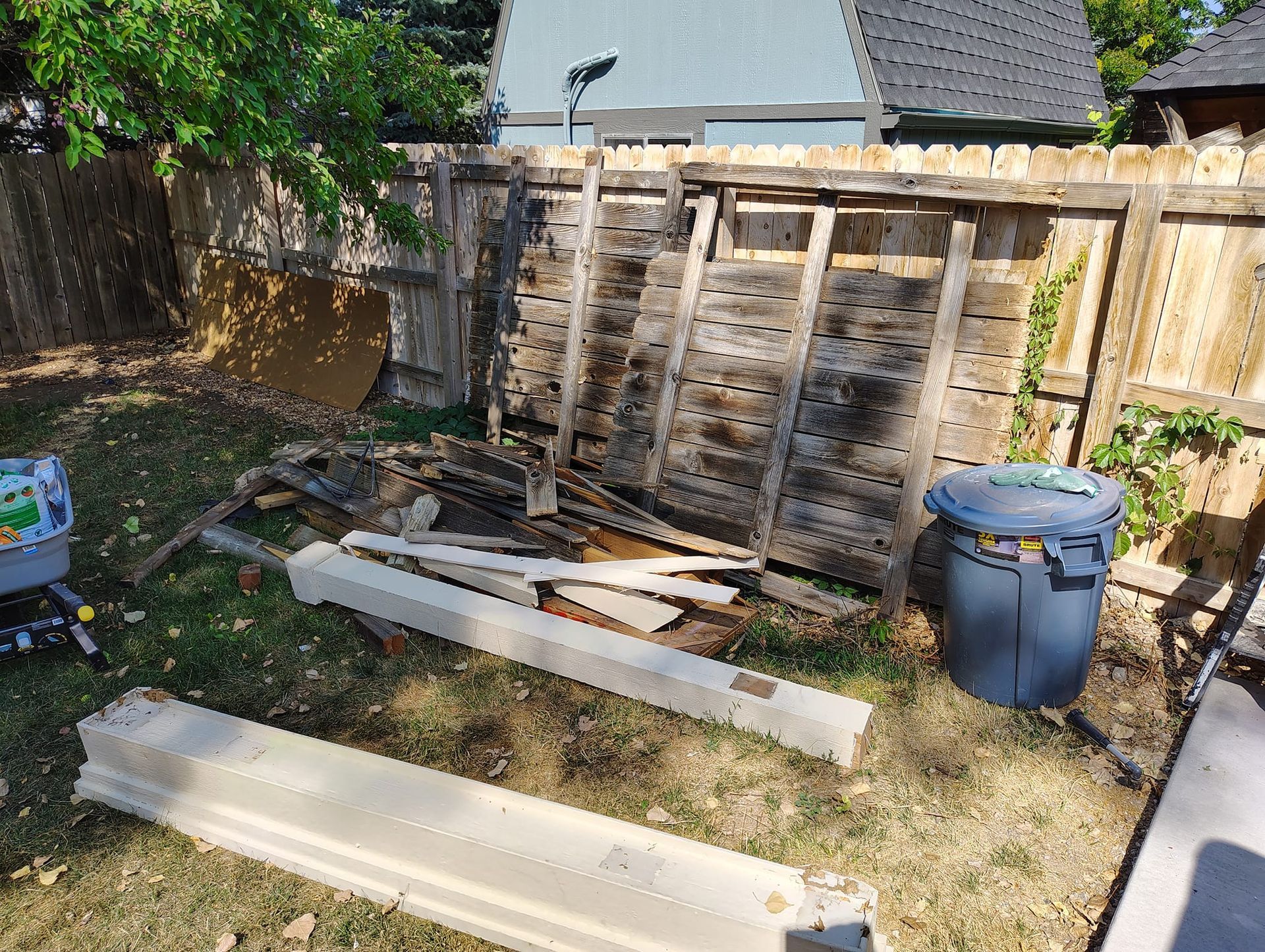 A pile of wood is sitting in the grass next to a wooden fence.