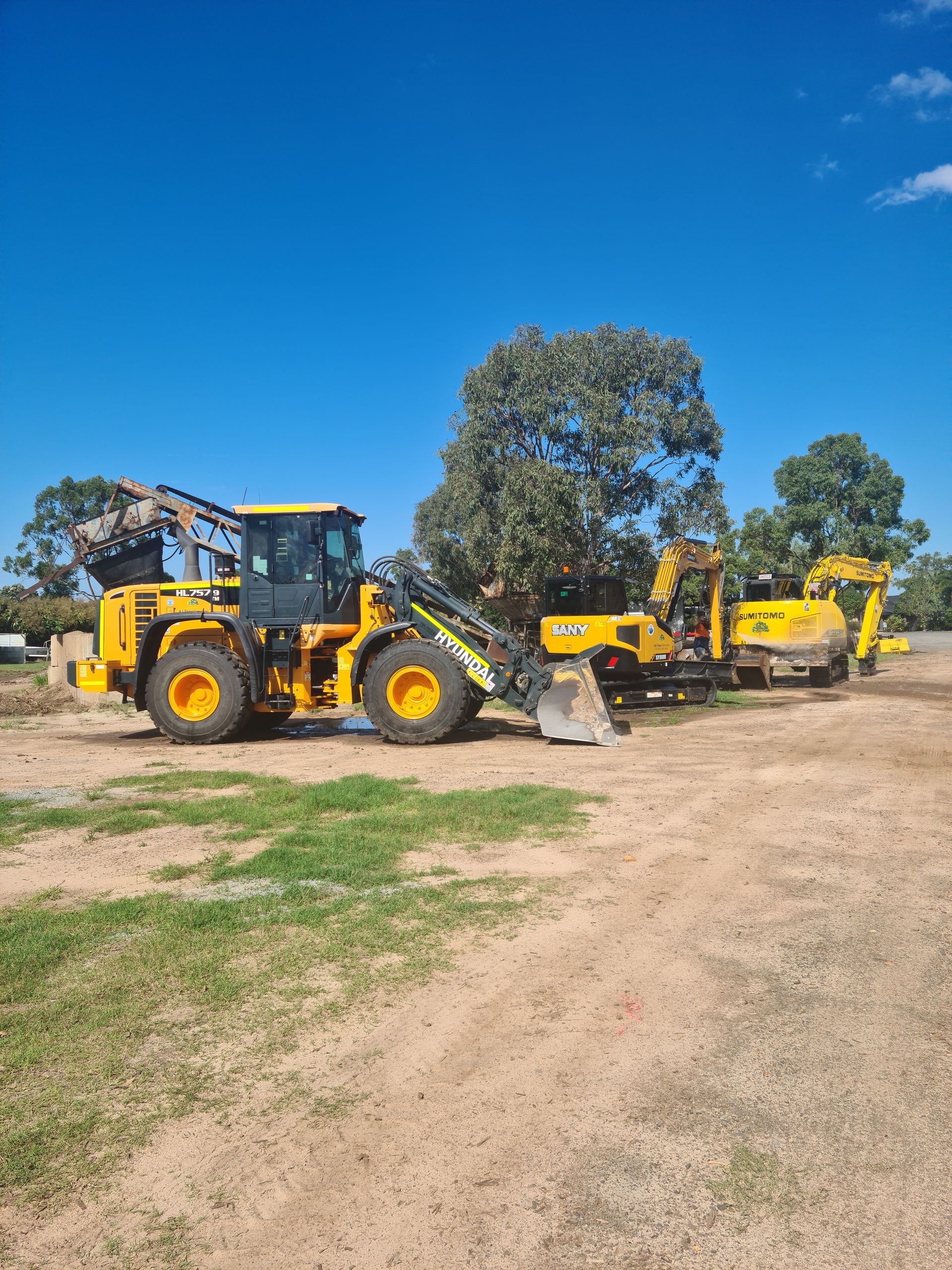 A White Dump Truck is Towing an Excavator on a Trailer — A1 Tree Service in Kensington, QLD
