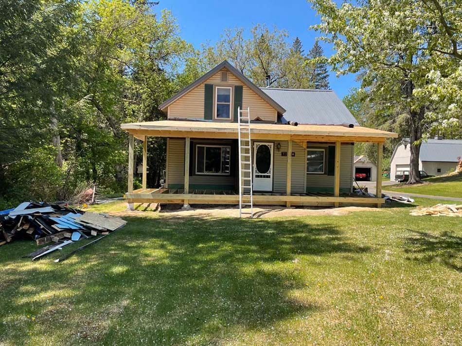 A house with a porch and a ladder in front of it.