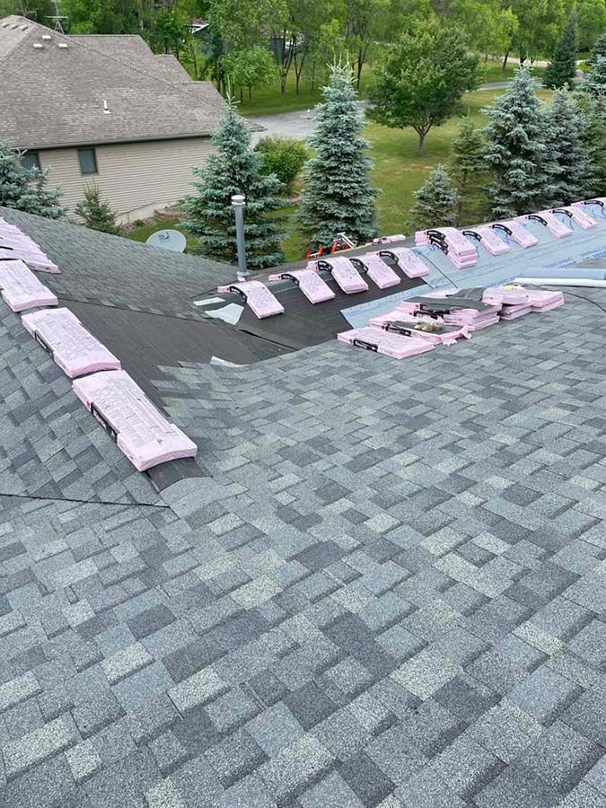 A roof with a lot of shingles on it and a house in the background.