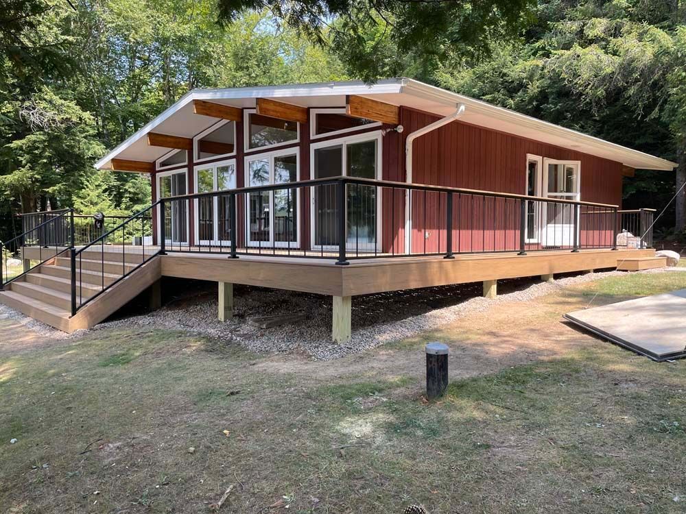 A red house with a large deck and stairs surrounded by trees.