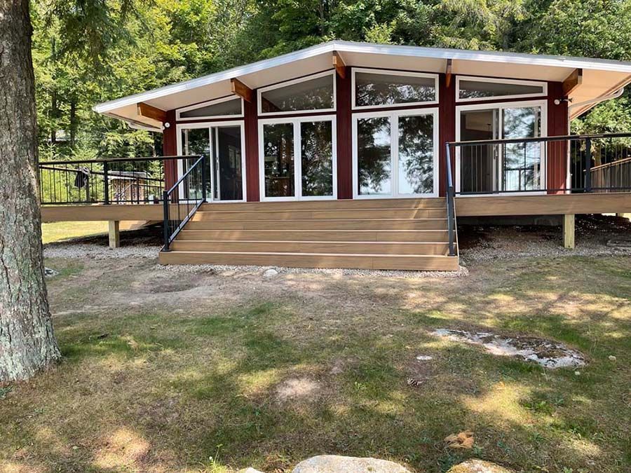 A house with a large deck and stairs is surrounded by trees.
