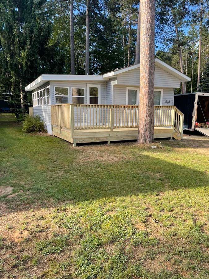A small white house with a wooden deck and a trailer parked in front of it.