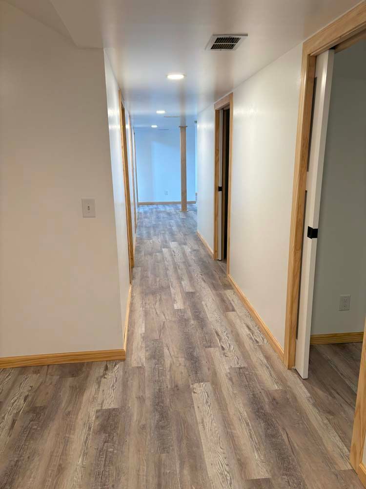 A long hallway with hardwood floors and white walls in a house.