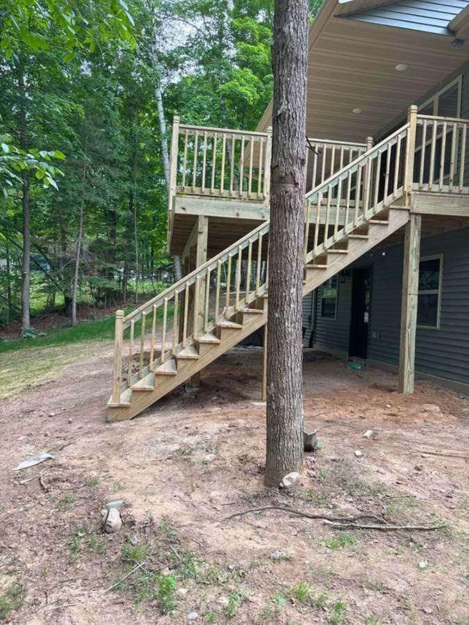 A wooden deck with stairs leading up to the second floor of a house.
