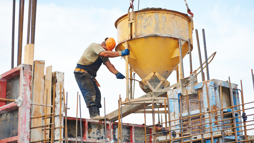 A construction worker is pouring cement into a bucket at a construction site.
