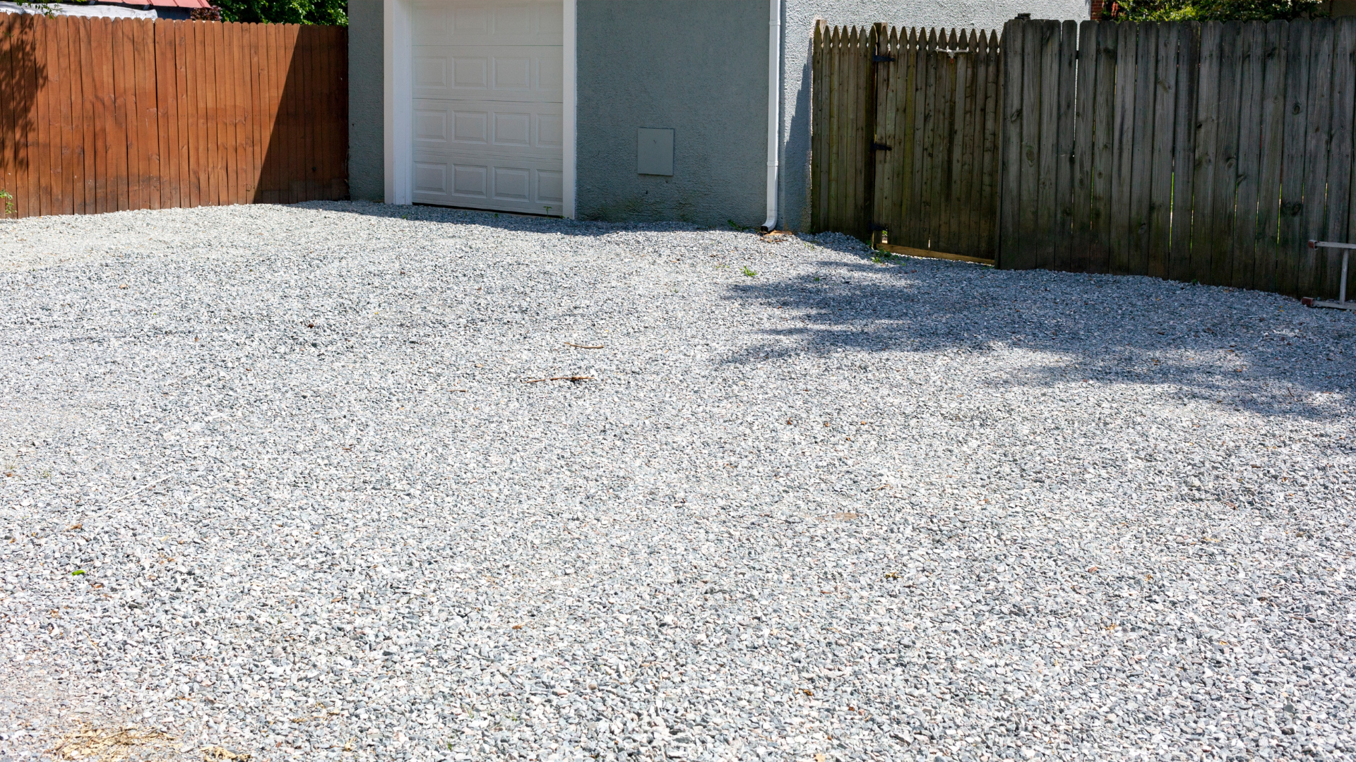 A gravel driveway with a wooden fence and a garage in the background.