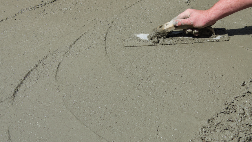 A person is spreading concrete on the ground with a trowel.
