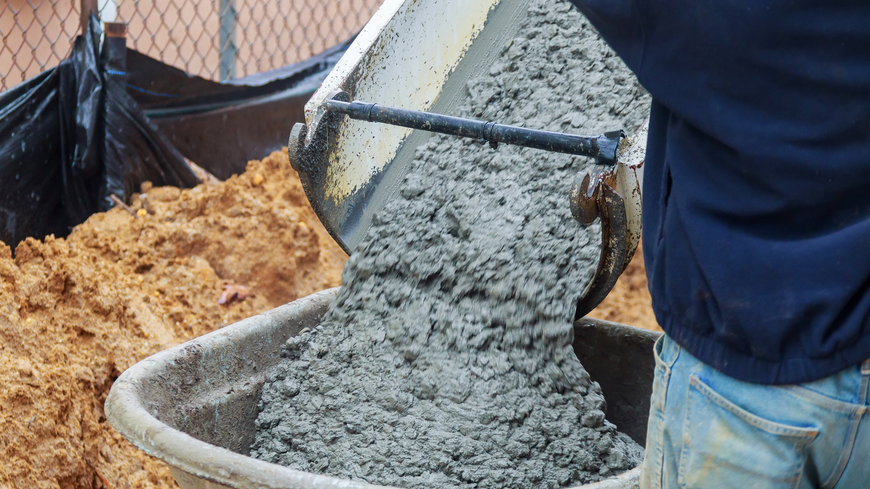 A man is pouring concrete into a wheelbarrow.