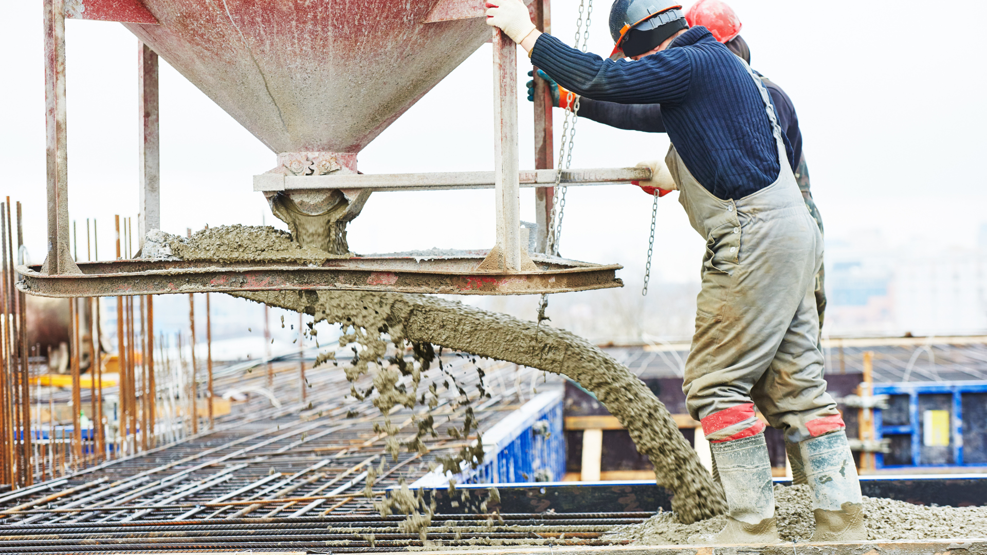 A man is pouring concrete from a bucket on a construction site.
