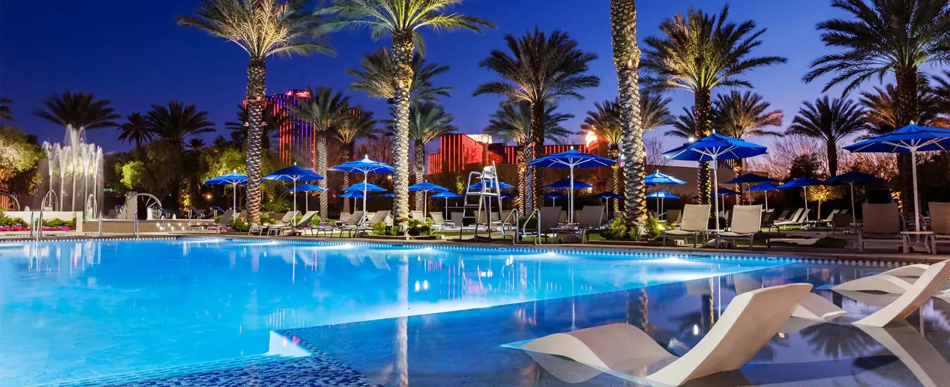 a large swimming pool surrounded by palm trees and umbrellas at night .