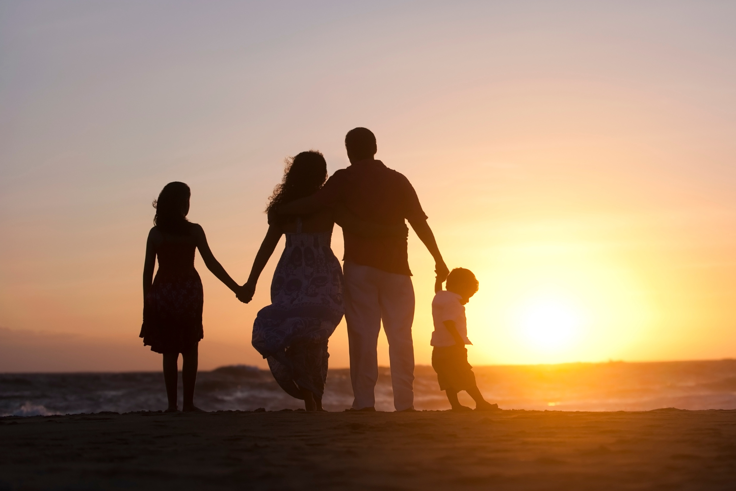 Family silhouetted on beach at sunset, holding hands.