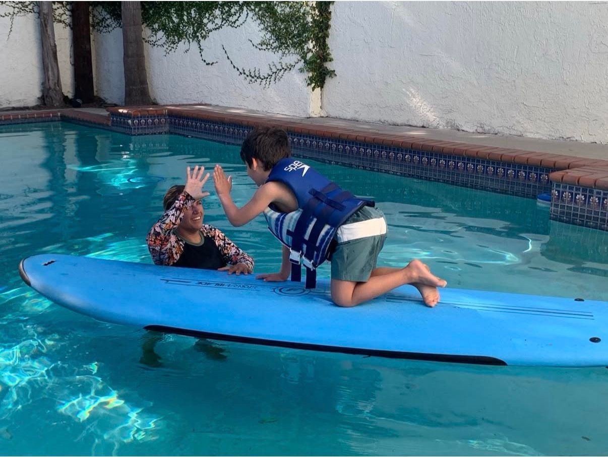 Woman teaching a child to surf on a blue board in a pool.