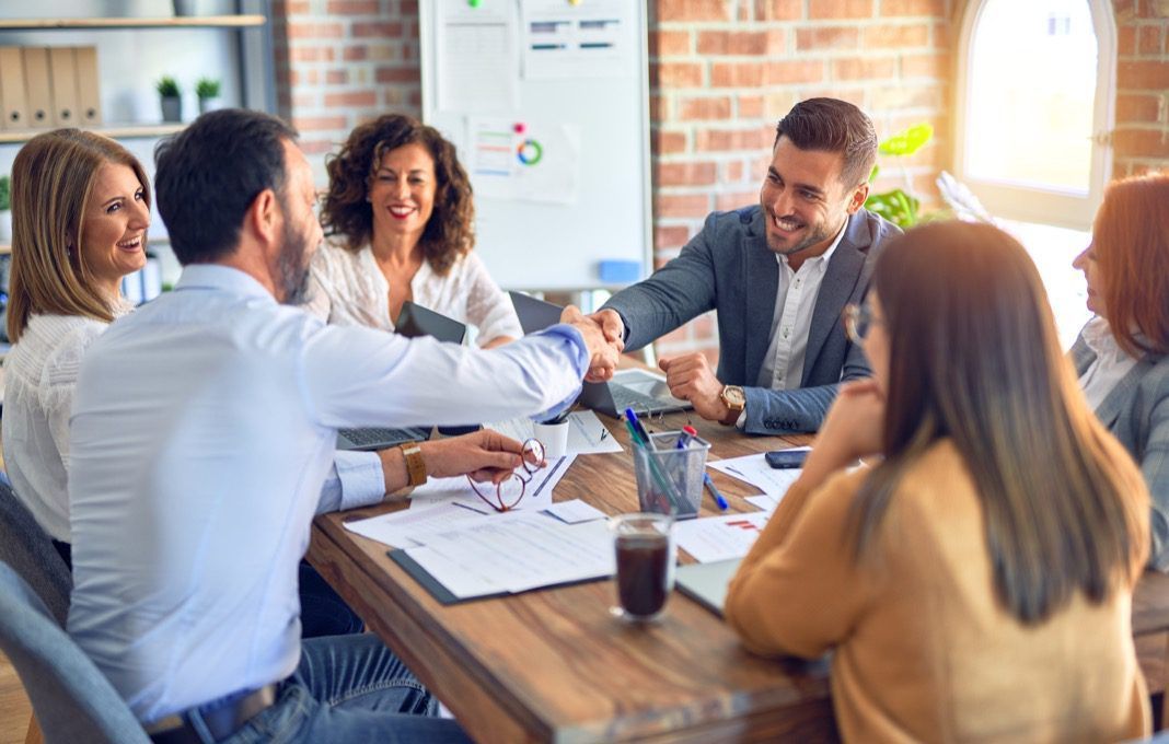 A group of people are sitting around a table shaking hands.
