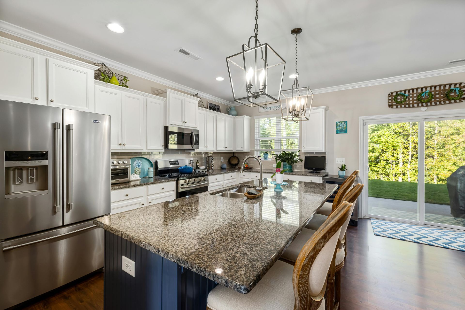 A kitchen with granite counter tops , stainless steel appliances , white cabinets and a large island.