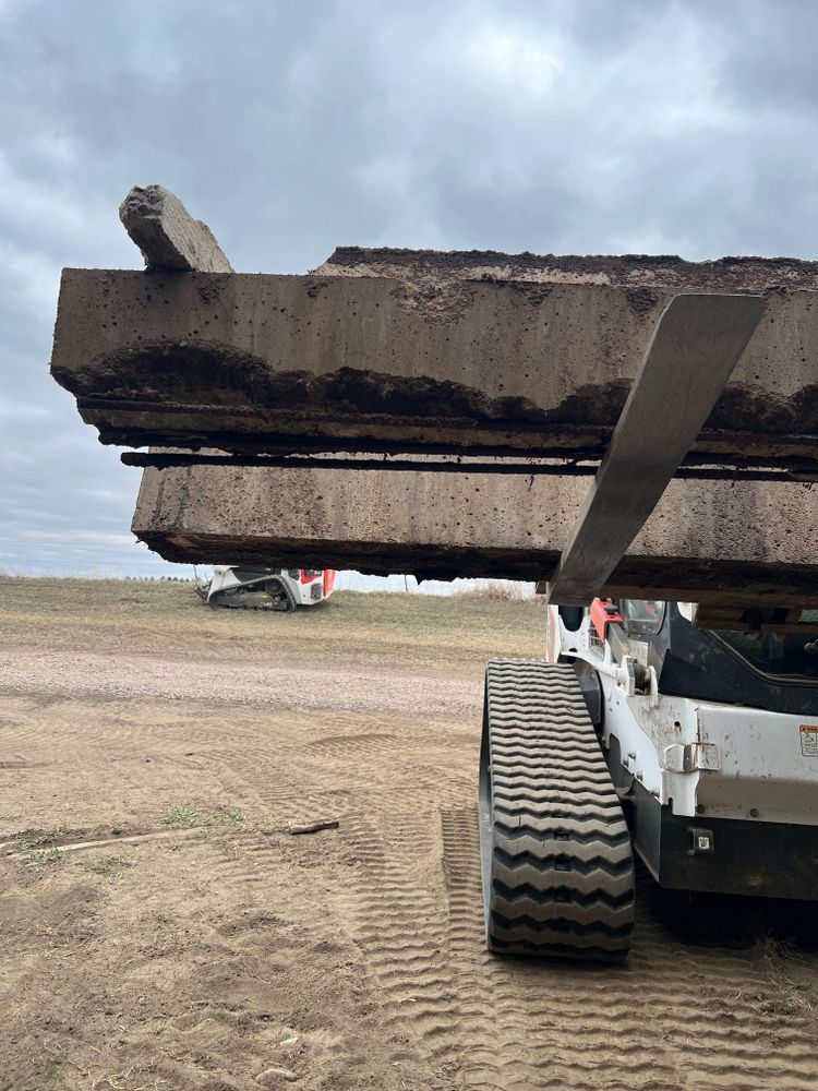 A bulldozer is carrying a stack of concrete slabs in a field.