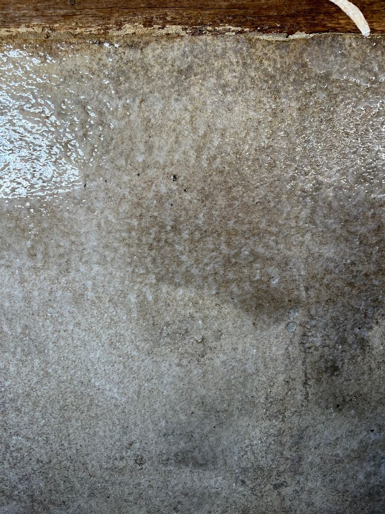 A close up of a concrete wall with a wooden beam in the background.