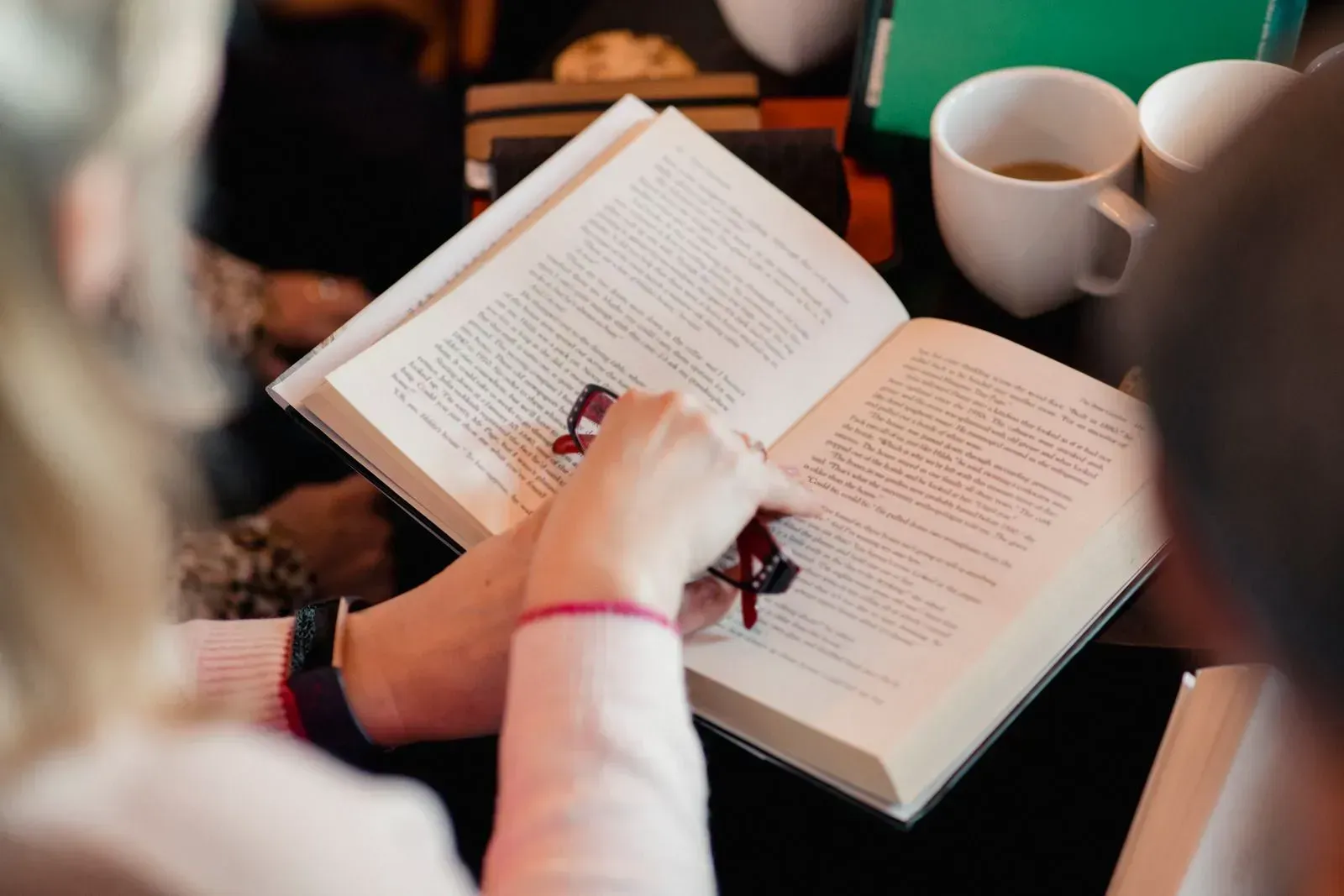 A woman is sitting at a table reading a book.