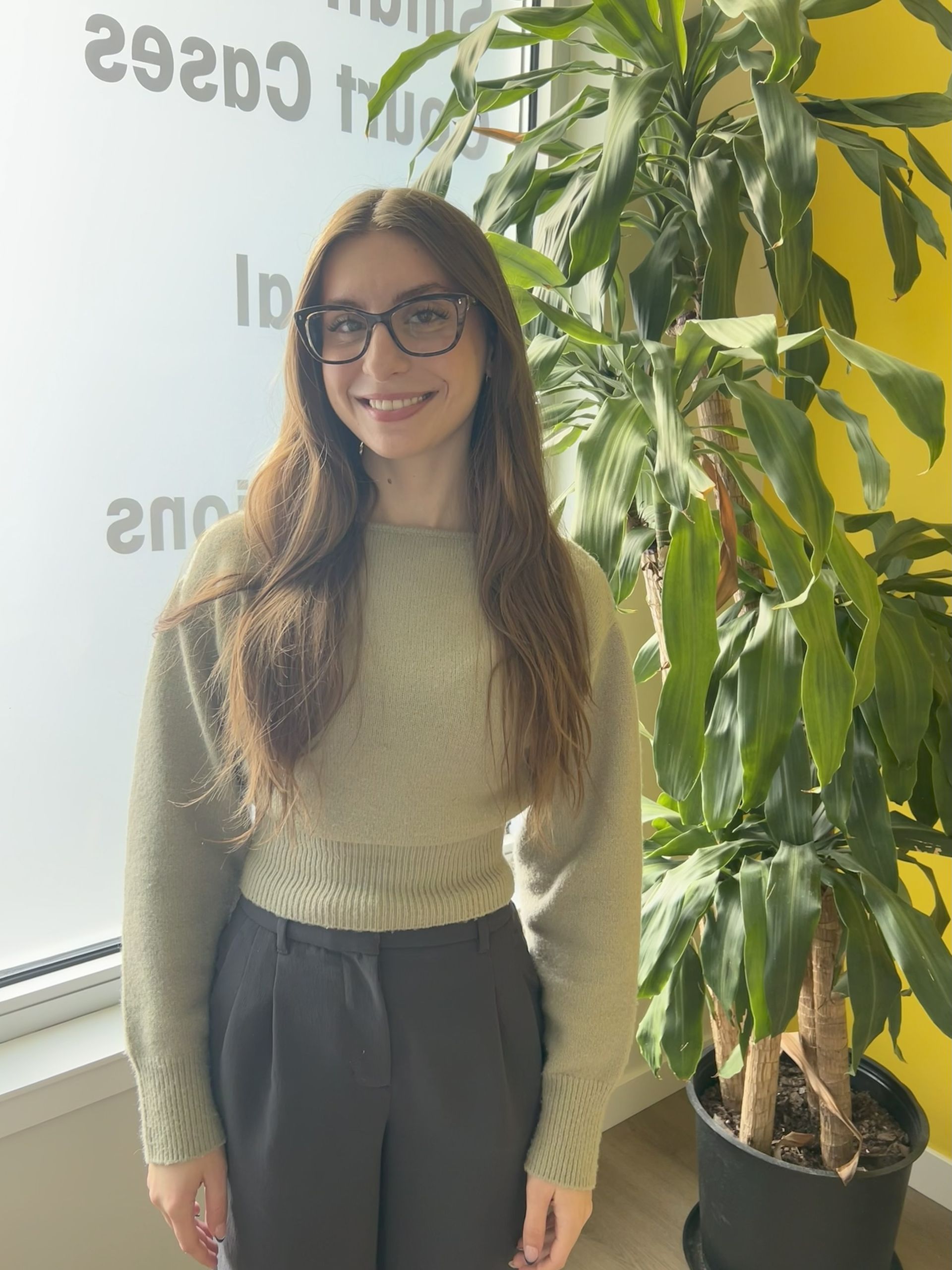 A woman with long blonde hair is standing in front of a window.