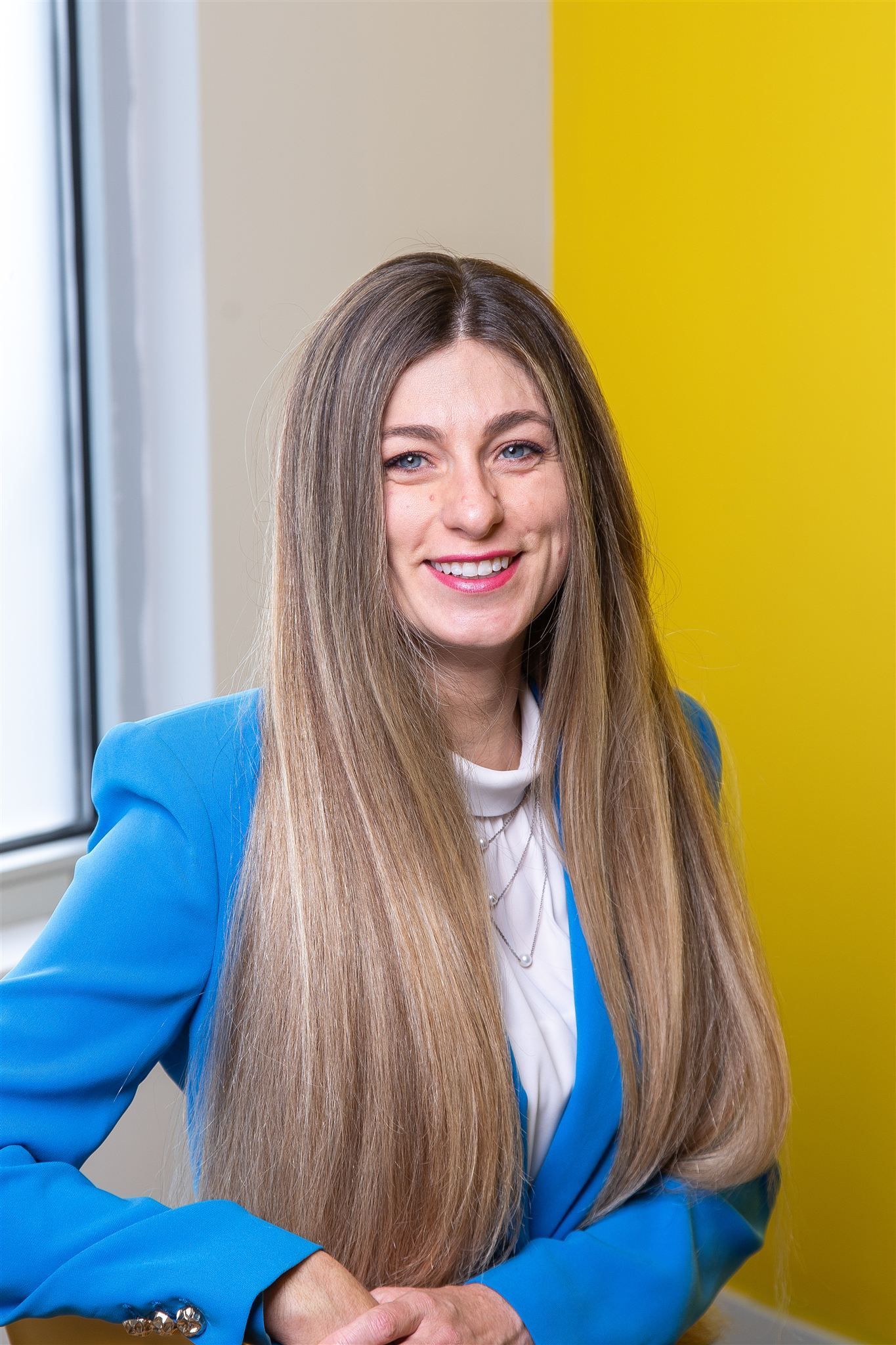 A woman with long blonde hair is standing in front of a window.