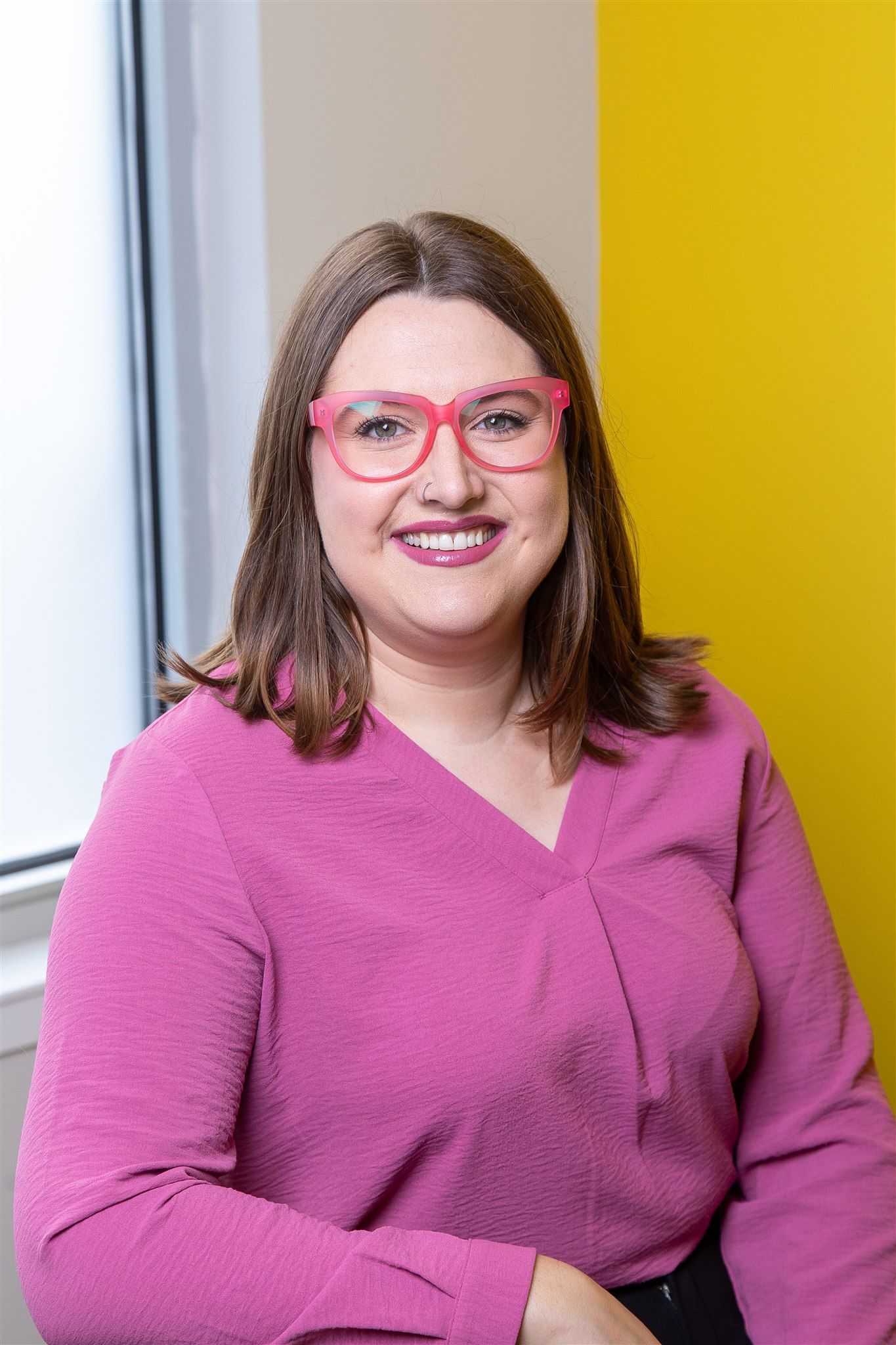 A woman with long blonde hair is standing in front of a window.
