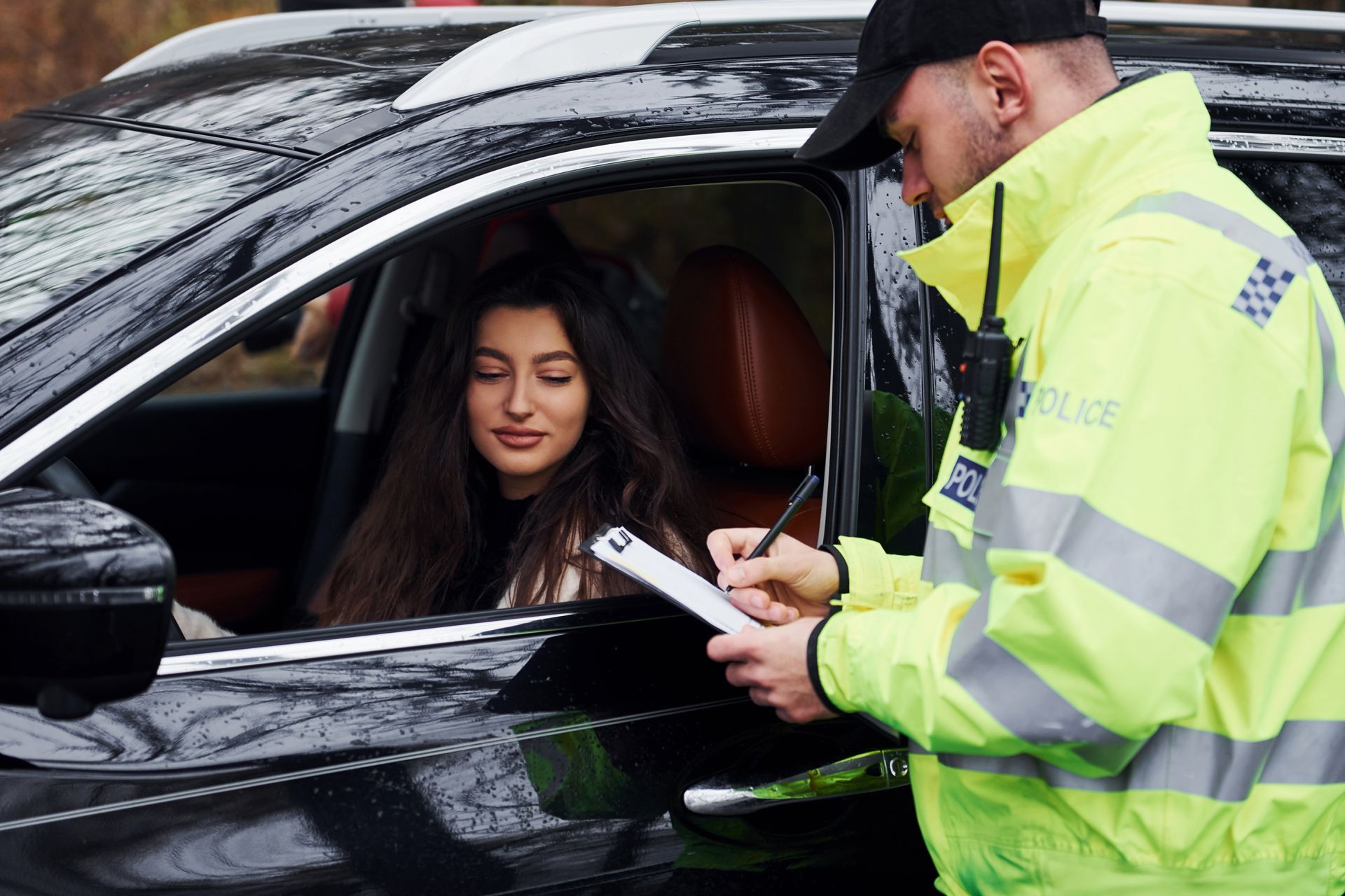 A police officer is writing a ticket to a woman in a car.