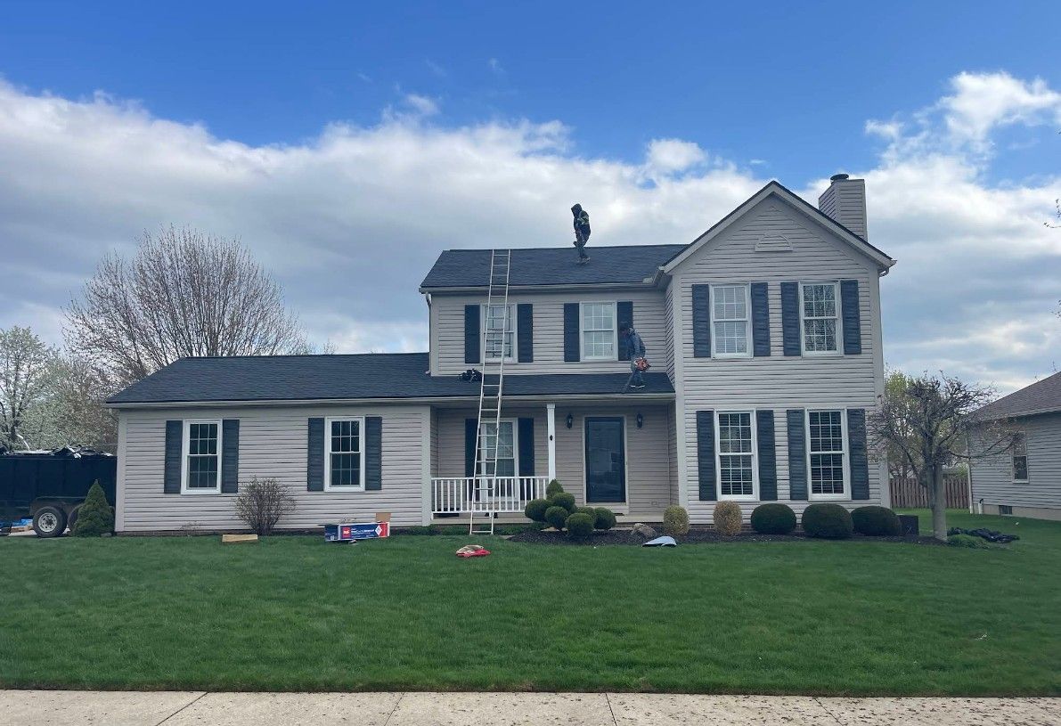 A man is standing on a ladder on the roof of a house.