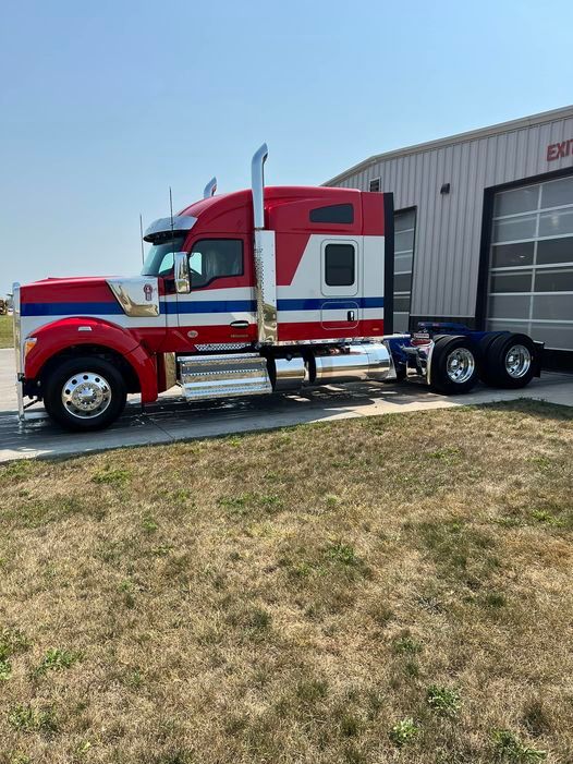 A red , white and blue semi truck is parked in front of a building.