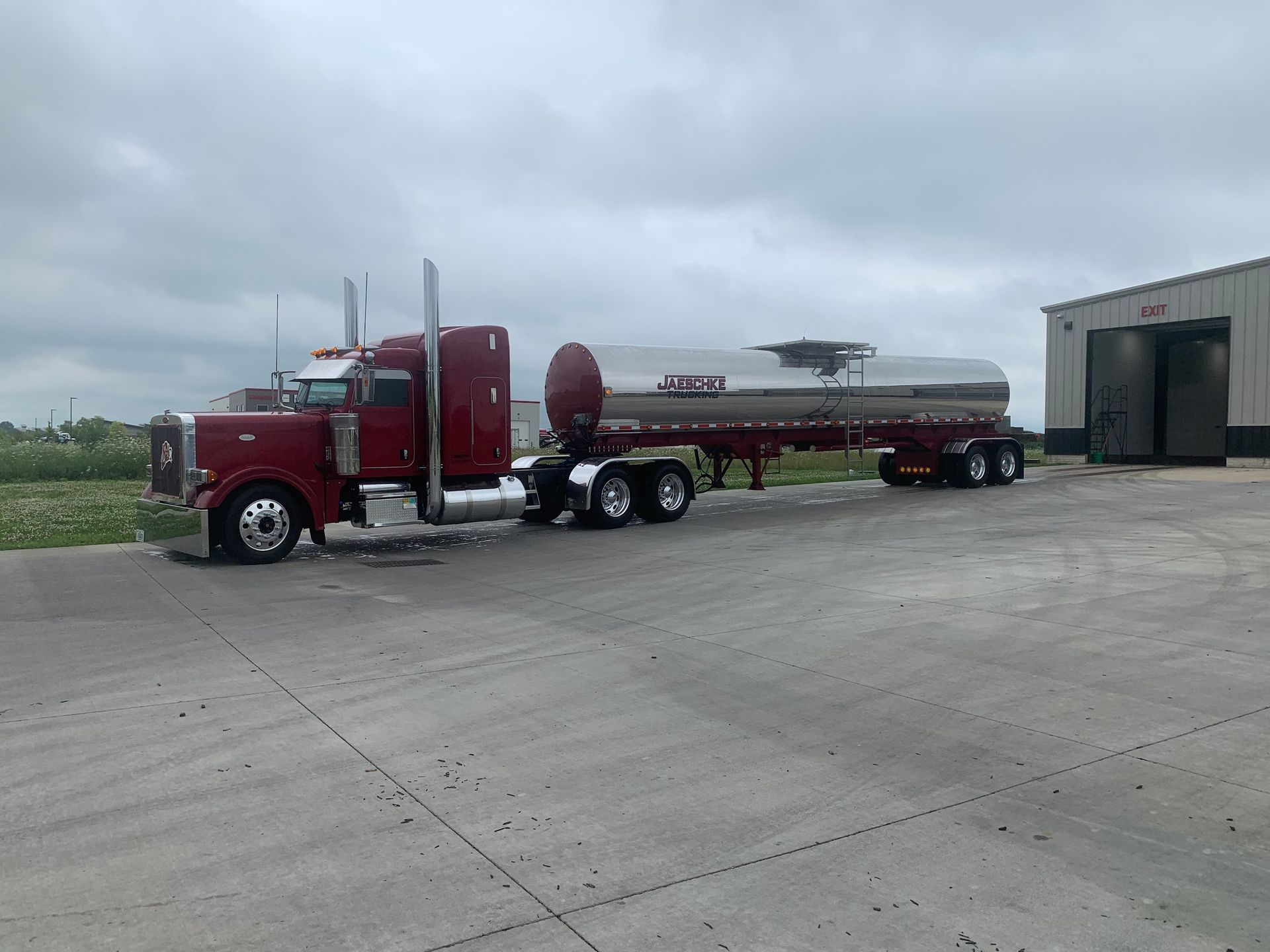 A red semi truck is parked in a parking lot next to a building.