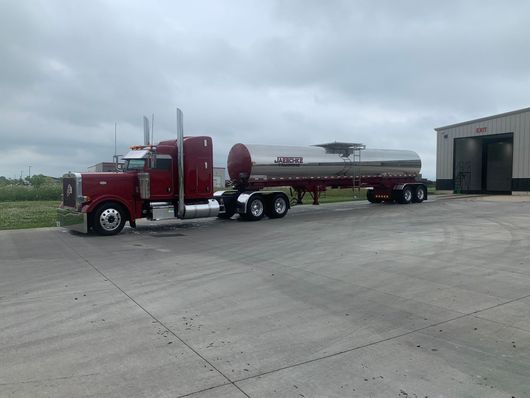 A red semi truck is parked in a parking lot next to a building.