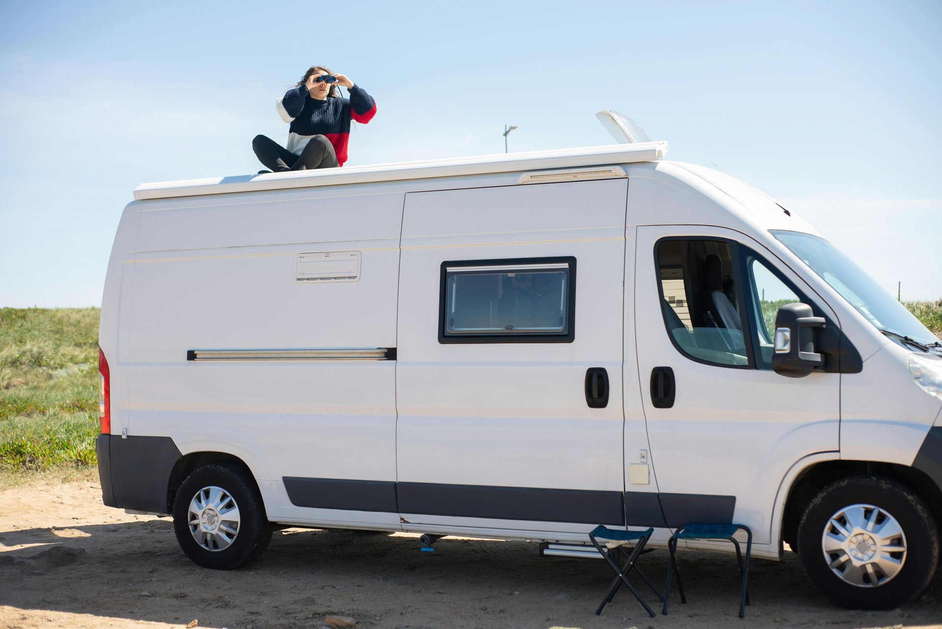 Person on a white van roof taking pictures in a field with blue sky.