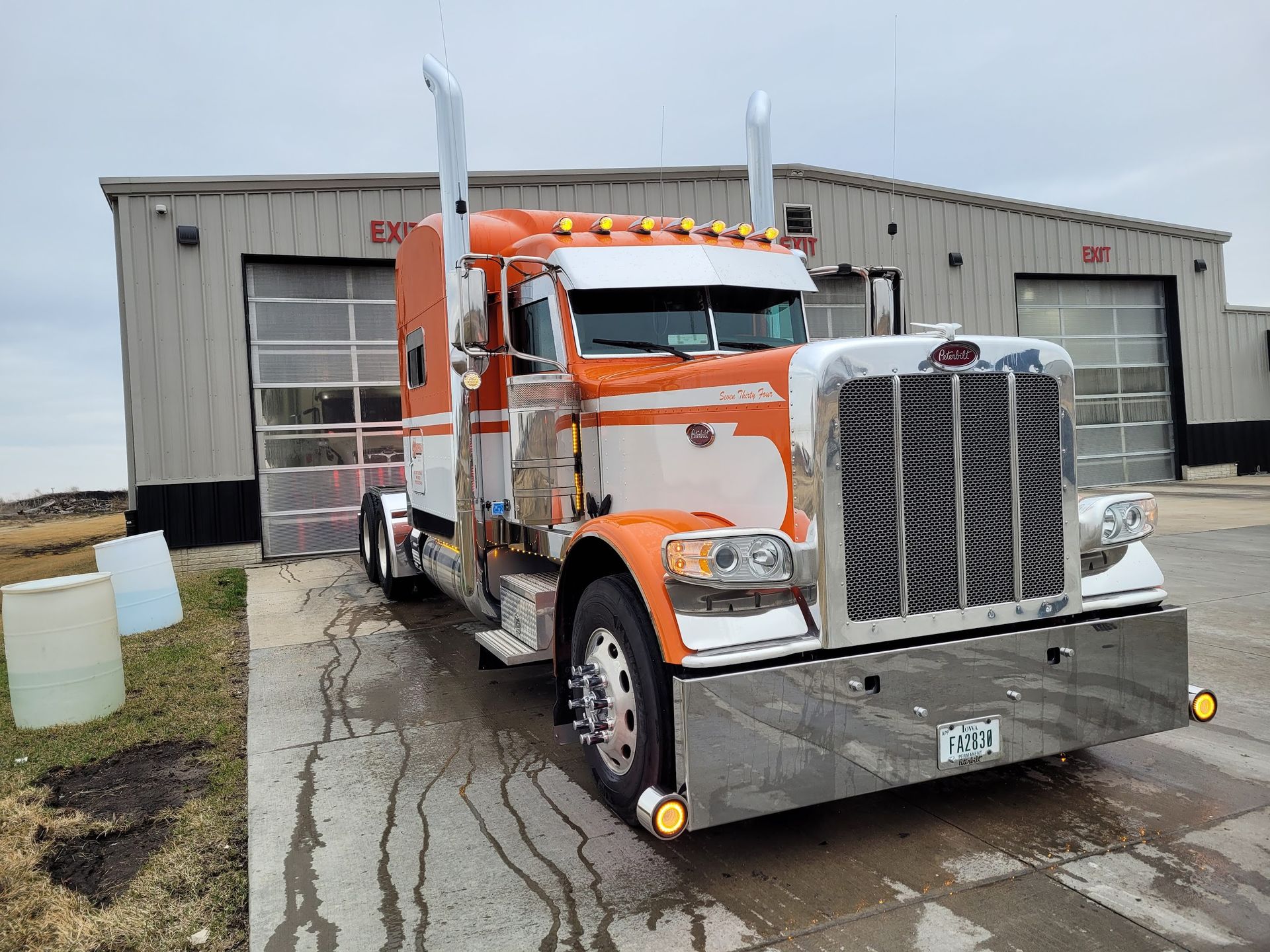 An orange and white semi truck is parked in front of a building.