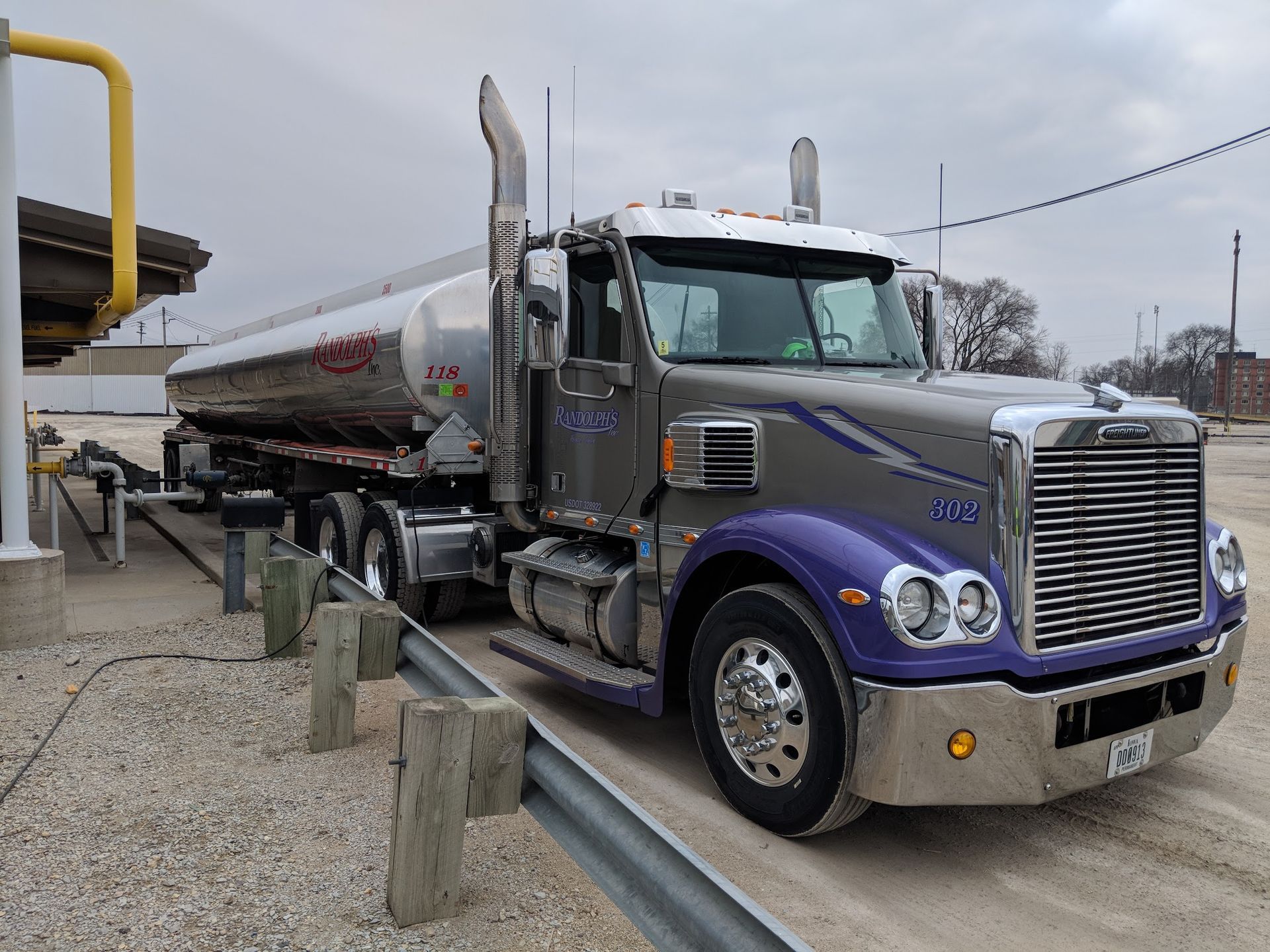 A purple and silver semi truck is parked in a gravel lot.