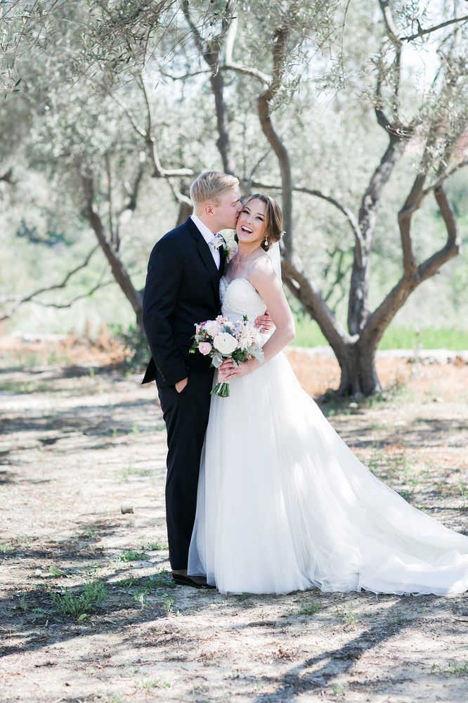 Bride and groom kiss under trees in a sunlit outdoor setting