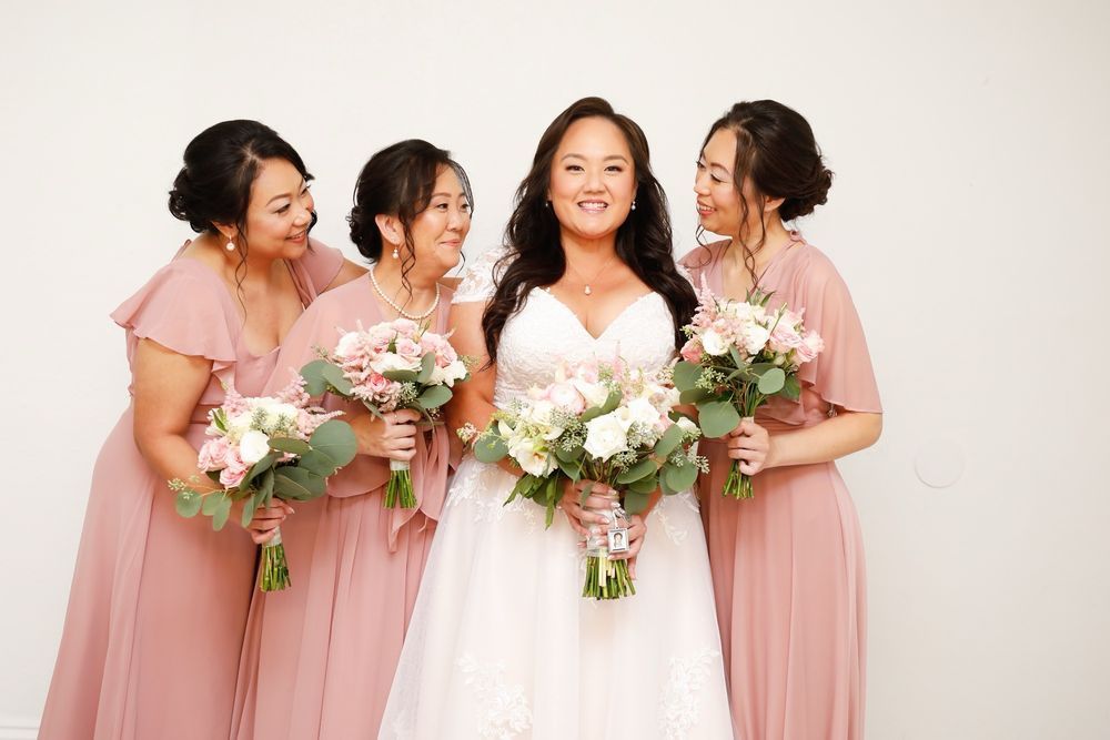 Bride in white dress with three bridesmaids in pink dresses holding bouquets and smiling