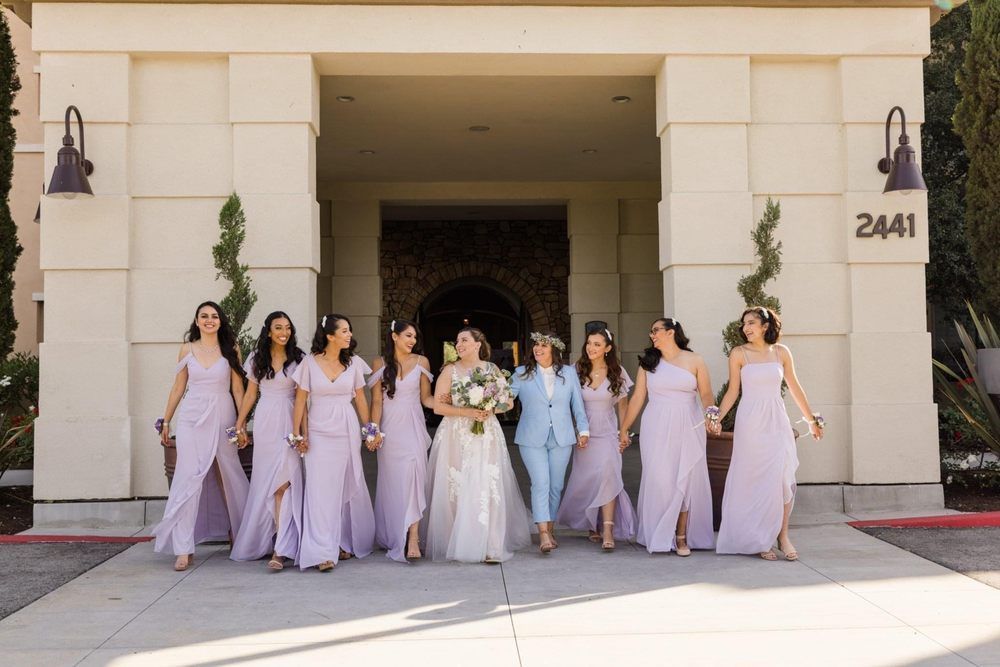Nine women in lavender dresses and one in white stand outside a building entrance with the number 2441.