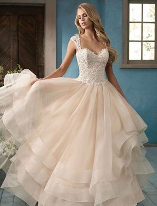 Woman in a white lace and blush tulle ball gown standing indoors by a window