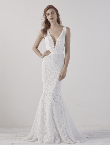 Woman in a white lace wedding dress standing against a neutral studio backdrop