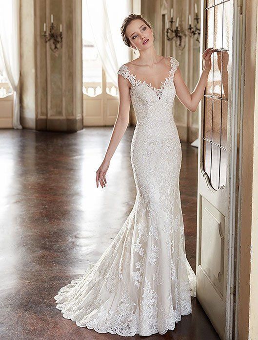 Woman in a white lace wedding dress standing in a sunlit room by a doorway